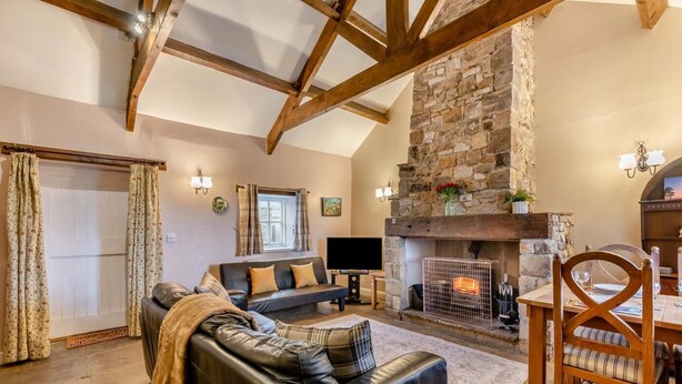 A cozy living room with a stone fireplace, a leather sofa, and a dining area with a wooden table and chairs. - 2 Bed in Eggleston (oc-s30453) (Middleton-in-Teesdale)