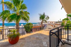 Un balcon avec un sol en pierre, des palmiers et une vue sur la mer.