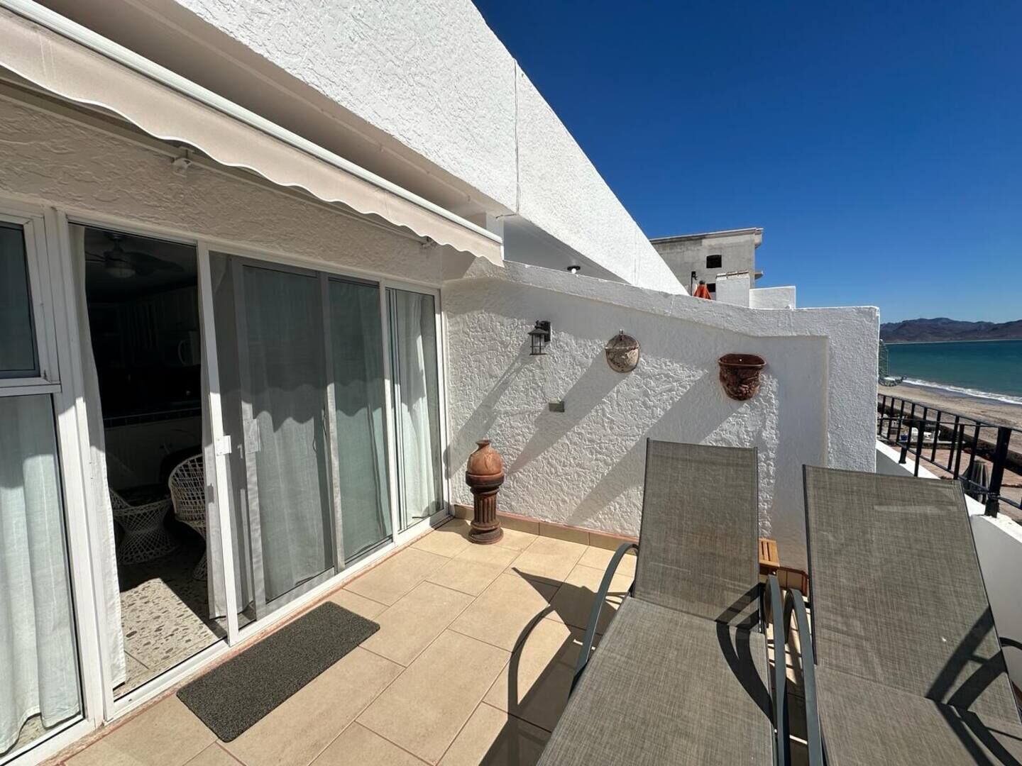 A balcony with a view of the sea, a white building, and a door with a basket inside.