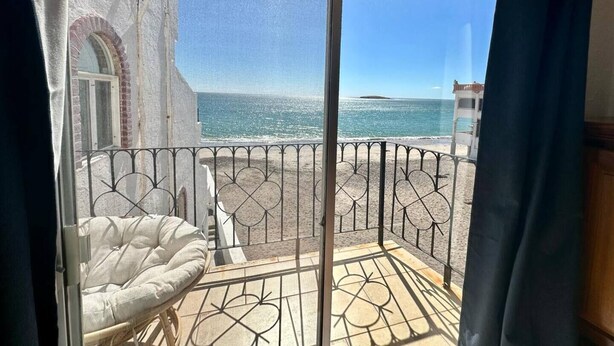 Een balkon met uitzicht op zee, een witte fauteuil met kussens en een metalen hekwerk.