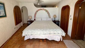 Een slaapkamer met een groot bed, een plafondventilator en een decoratieve bloemrijke boog.
