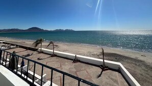 Uitzicht op een strand vanaf een balkon, met een heldere lucht, een zandstrand en een rustige zee.