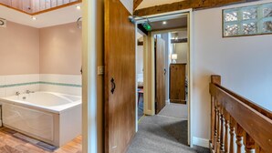 Une salle de bain avec une grande baignoire, une porte en bois et un couloir menant à une autre pièce.