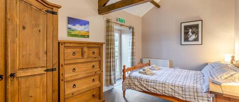 Een slaapkamer met een houten dressoir, een bed met geruit beddengoed, een ingelijst schilderij en een raam met gordijnen.