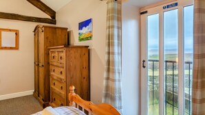 Une chambre à coucher avec un lit en bois, une armoire, un tableau et un balcon donnant sur la campagne.