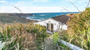 A coastal house with a view of the ocean, a wooden deck, and a pathway leading to the entrance.