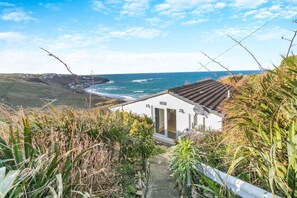 A coastal house with a view of the ocean, a wooden deck, and a pathway leading to the entrance. - 2 Bed in Sennen (oc-t30543) (Sennen)