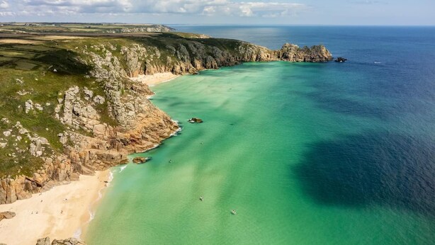 A coastal landscape with a clear view of the sea, rocky cliffs, and a sandy beach.