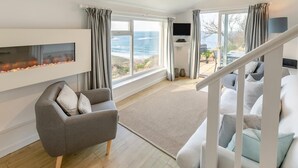 A modern living room with a sofa, a fireplace, a TV, and a view of the ocean.