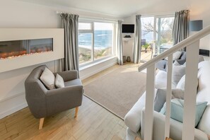 A modern living room with a sofa, a fireplace, a TV, and a view of the ocean. - 2 Bed in Sennen (oc-t30543) (Sennen)