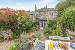 A stone house with a garden, a patio table with a meal set, and a bench. - 2 Bed in Newlyn (oc-t30565) (Newlyn)