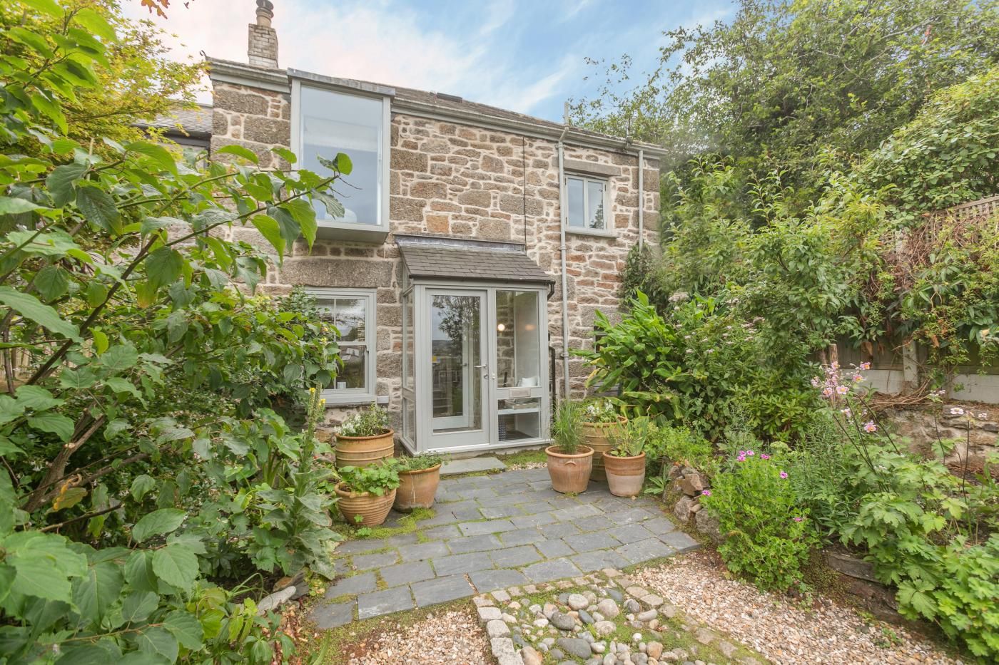 A stone house with a paved garden path leading to a glass door entrance.