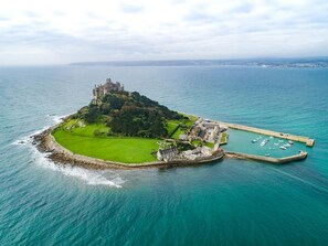 Vue aérienne d’un château situé sur une petite île, avec un port de plaisance et un port fortifié.