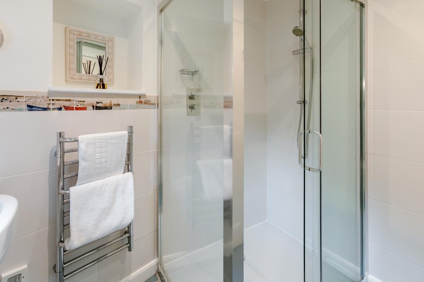 Une salle de bain moderne avec une douche à parois de verre, un porte-serviettes avec deux serviettes et un miroir avec éclairage intégré.