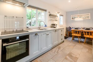 A modern kitchen with a built-in oven, a sink, and a dining area with a table and chairs. - 2 Bed in Newlyn (oc-t30565) (Newlyn)