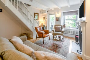 Un salon comprenant un escalier, un canapé, deux fauteuils, une table basse et un téléviseur.