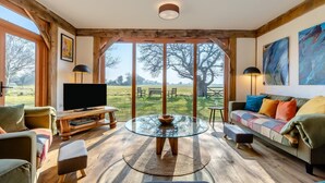 A spacious living room with a large window, a round glass table, and a sofa. - 3 Bed in Mundesley (oc-o30555) (Mundesley)