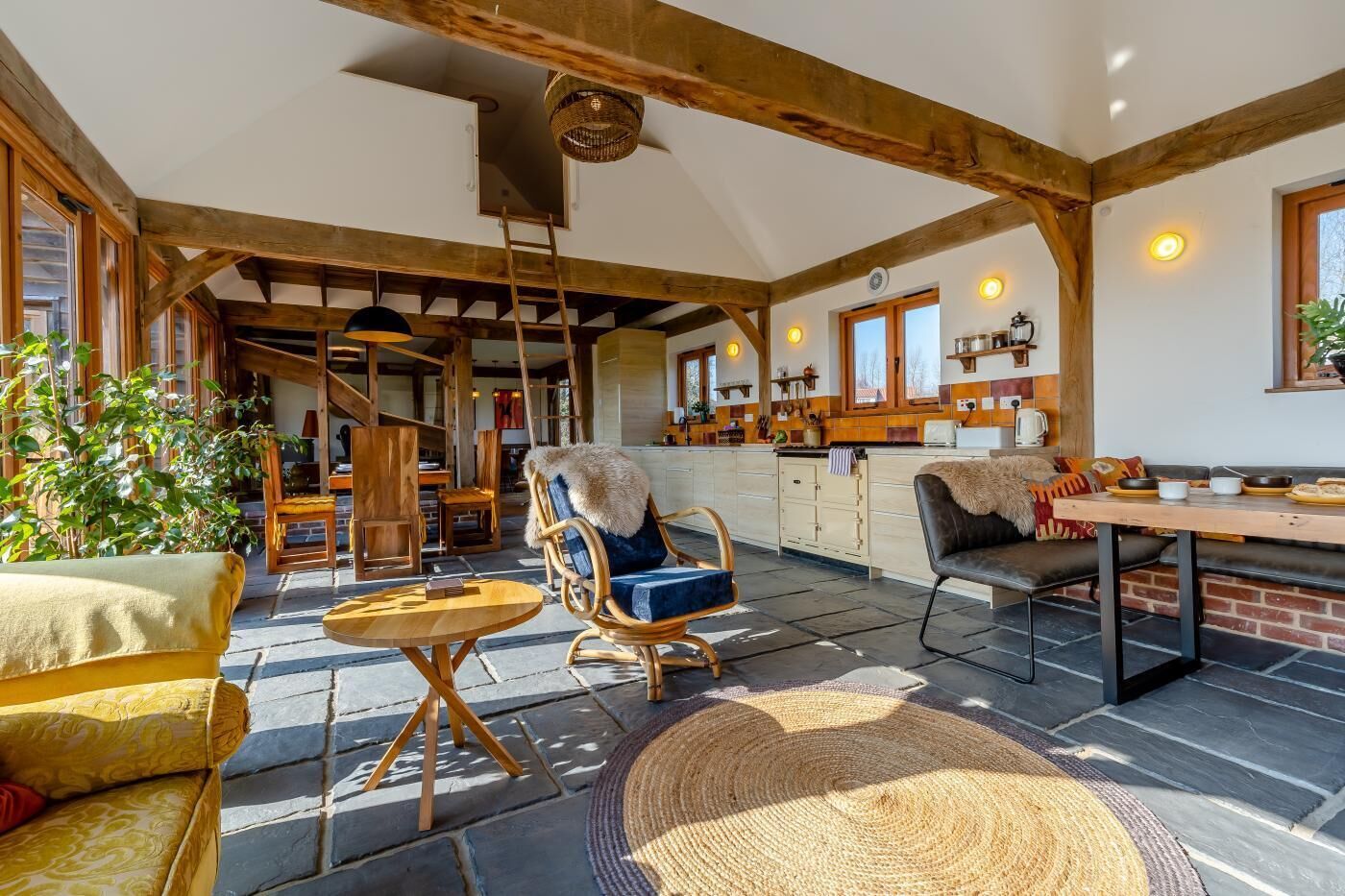 A spacious living area with a high ceiling, exposed wooden beams, a central seating area with a round table, and a kitchen in the background.