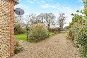 A gravel path leading to a house with a stone wall, a satellite dish, and a wooden fence. - 2 Bed in Briston (oc-s30561) (Briston)