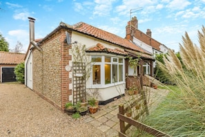 A two-story house with a brick exterior, a tiled roof, and a garden with potted plants.