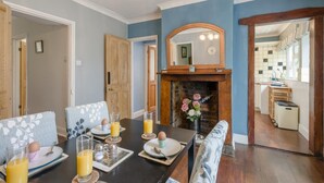 A dining area with a table set for breakfast, a fireplace, and a view into the kitchen.