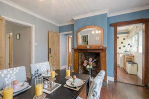 A dining area with a table set for breakfast, a fireplace, and a view into the kitchen.