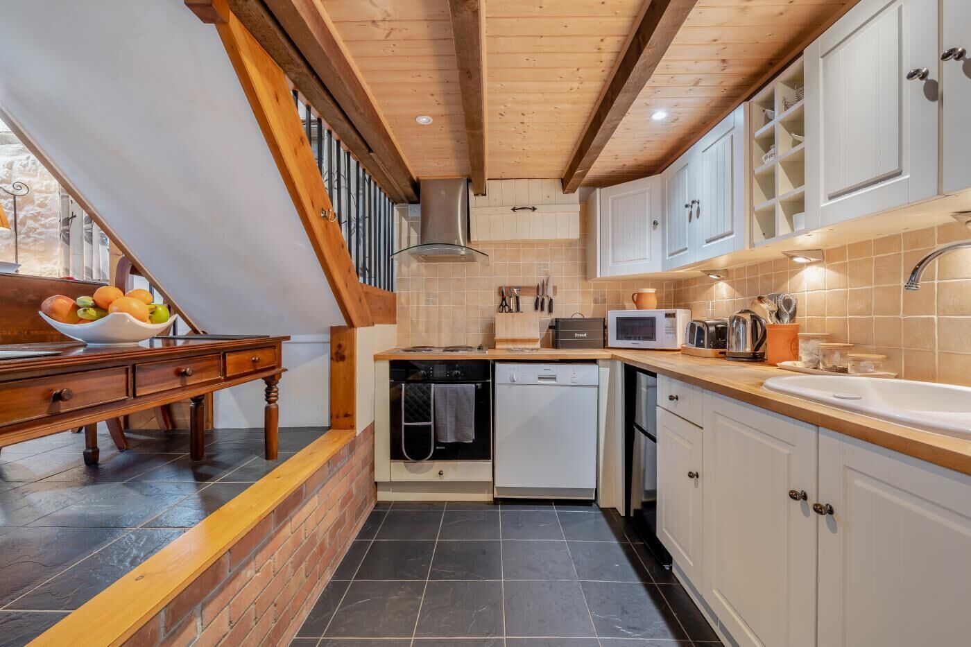 Una cocina con escalera de madera, armarios blancos y salpicadero de azulejos.