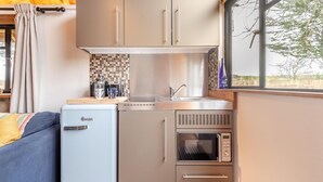 A compact kitchen with a refrigerator, microwave, and stove, a window with a view, and a small seating area with a sofa. - 1 Bed in Swanage (oc-l30493) (Harman's Cross)