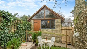 A small stone house with a wooden door and windows, surrounded by a garden with a table and chairs. - 1 Bed in Swanage (oc-l30493) (Harman's Cross)