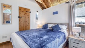 A bedroom with a bed, a wooden door, a wall-mounted light, and a window with curtains. - 1 Bed in Swanage (oc-l30493) (Harman's Cross)