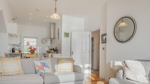 Ein modernes Wohnzimmer mit einer Couch, einem Couchtisch und einem Essbereich, im Hintergrund eine Küche.