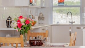 Eine moderne Küche mit weißen Schränken, einem gedeckten Esstisch mit Tellern und Gläsern, einer Blumenvase und Blick ins Freie durch ein Fenster.
