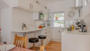 Eine moderne Küche mit weißen Schränken, einer Kaffeemaschine, einer Mikrowelle und einem Fenster mit Jalousien.