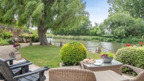 A patio with wicker furniture, a stone table, and a view of a river and greenery. - 4 Bed in Wareham (oc-r30563) (Wareham)