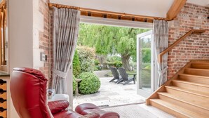 A room with a red leather chair, a wooden staircase, and a view of a garden with a table and chairs outside. - 4 Bed in Wareham (oc-r30563) (Wareham)