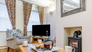 Ein gemütliches Wohnzimmer mit einer Couch, einem Couchtisch mit Gebäck, einem Fernseher und einem Kaminofen.