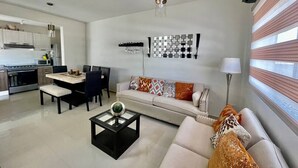 Een moderne woonkamer met een bank, eettafel en stoelen. Er is een keuken met apparatuur en een magnetron.