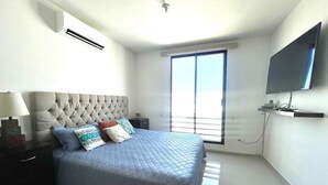 Een slaapkamer met een bed, nachtkastje, televisie en raam.