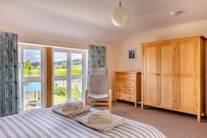 A bedroom with a bed, a chair, a wooden wardrobe, and a window with curtains. - 3 Bed in Burton Bradstock (oc-c30570) (Burton Bradstock)