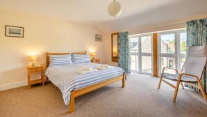 Een slaapkamer met een bed, nachtkastjes, een stoel en uitzicht door een groot raam.