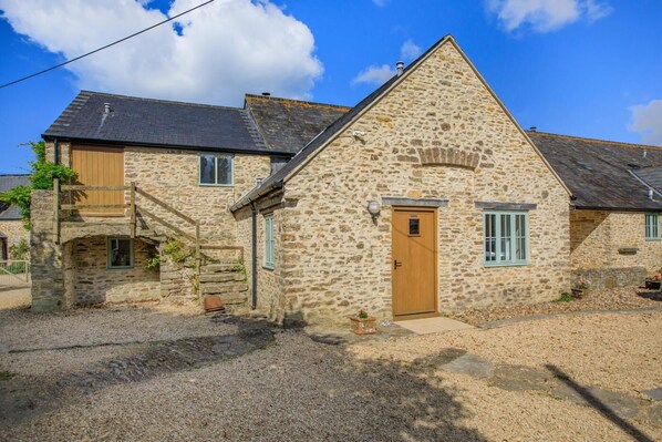 A stone building with a wooden door, a small window, and a staircase leading to a wooden platform. - 3 Bed in Burton Bradstock (oc-c30570) (Burton Bradstock)