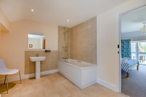 A modern bathroom with a bathtub, shower, and sink. - 3 Bed in Burton Bradstock (oc-c30570) (Burton Bradstock)