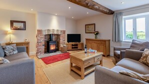 A living room with a fireplace, sofas, a coffee table, a TV, and a window with curtains. - 3 Bed in Burton Bradstock (oc-s30572) (Burton Bradstock)