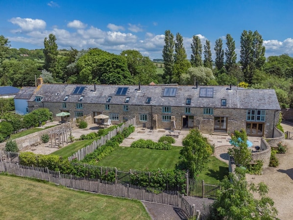 A stone building with multiple rooms, a fenced garden, and a clear sky. - 3 Bed in Burton Bradstock (oc-s30572) (Burton Bradstock)