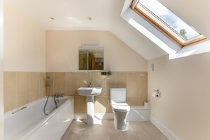 Ein modernes Badezimmer mit Oberlicht, einer Badewanne, einem Waschbecken und einer Toilette.