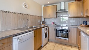 A modern kitchen with a dishwasher, washing machine, oven, and a stainless steel range hood. - 3 Bed in Burton Bradstock (oc-s30572) (Burton Bradstock)