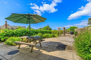 Eine Terrasse im Freien mit einem Holztisch und einer Bank, einem grünen Sonnenschirm und einem Grill.