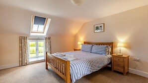 A bedroom with a skylight, a bed with striped bedding, two bedside tables with lamps, and a framed picture on the wall. - 3 Bed in Burton Bradstock (oc-s30572) (Burton Bradstock)
