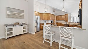 Une cuisine moderne avec des meubles en bois, un réfrigérateur en acier inoxydable et un coin bar agrémenté de tabourets blancs.