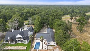 Une grande maison avec une piscine, entourée d’une forêt dense et de vastes champs.